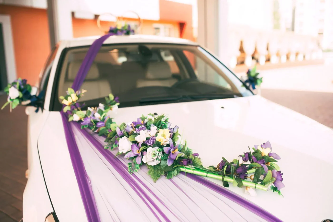 White wedding car styled with purple ribbon and flowers