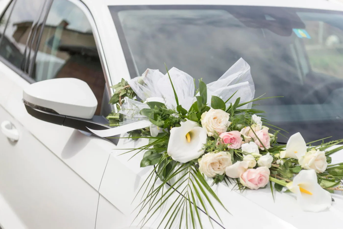 Pink and ivory roses with greenery arranged on a white car bonnet