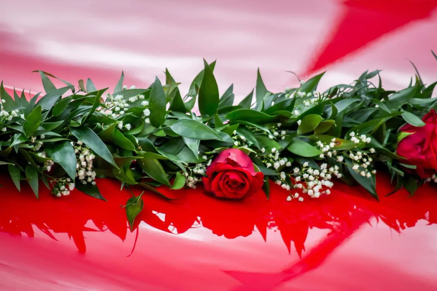Red roses and greenery laid across a red wedding car bonnet
