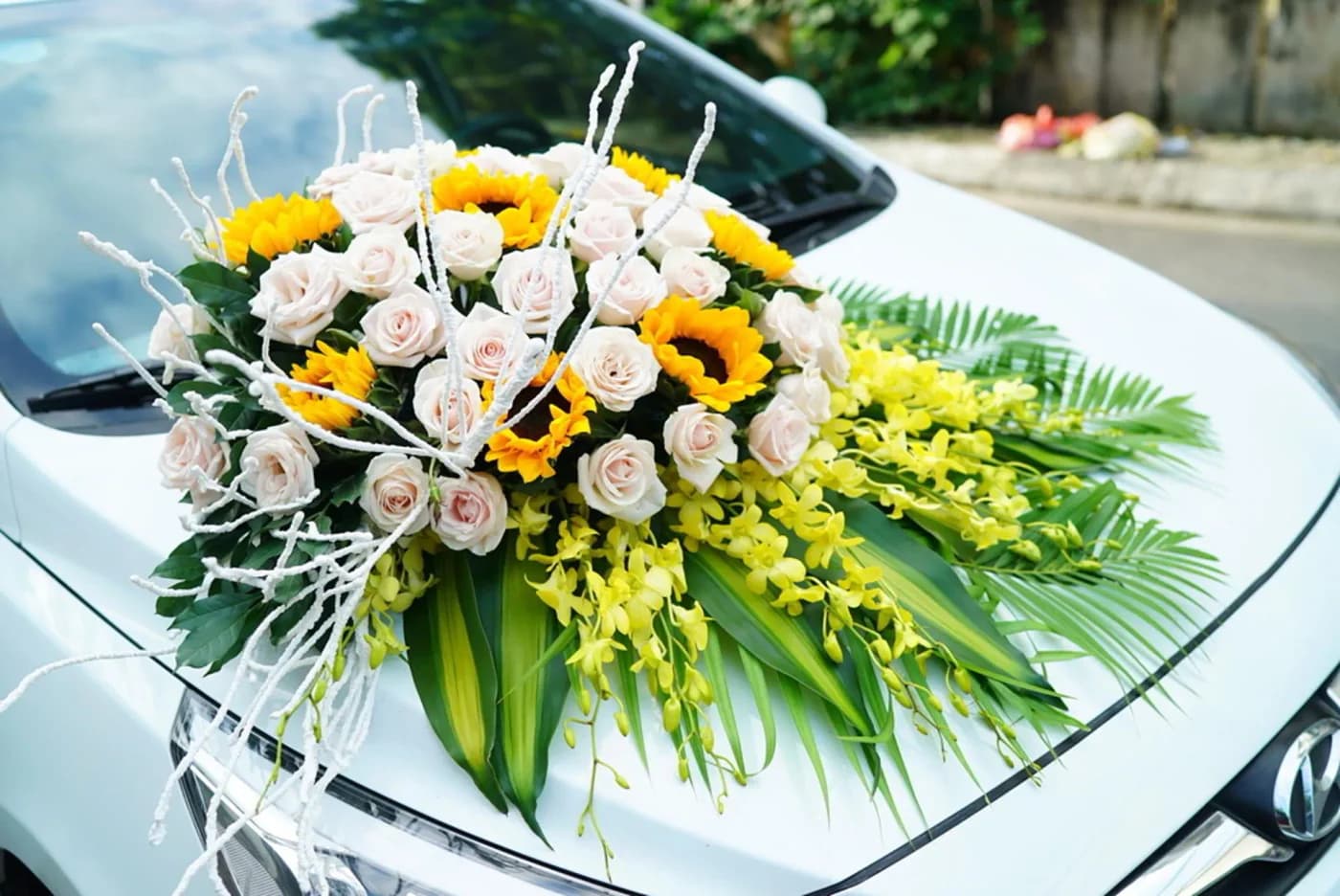 White and yellow flowers with greenery on a white car bonnet