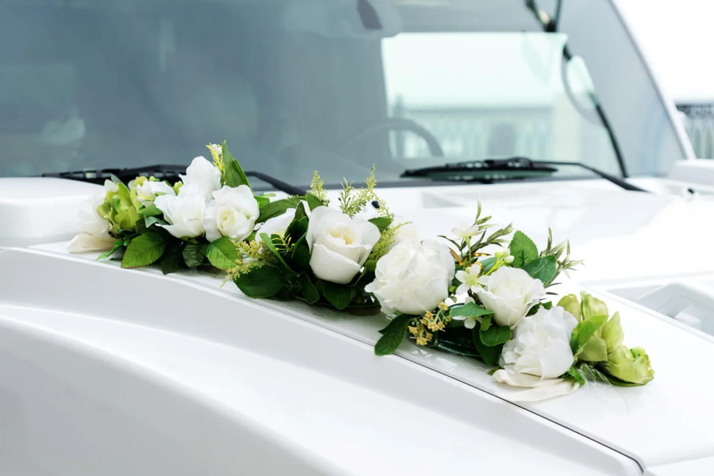 White roses and greenery on a white wedding car bonnet