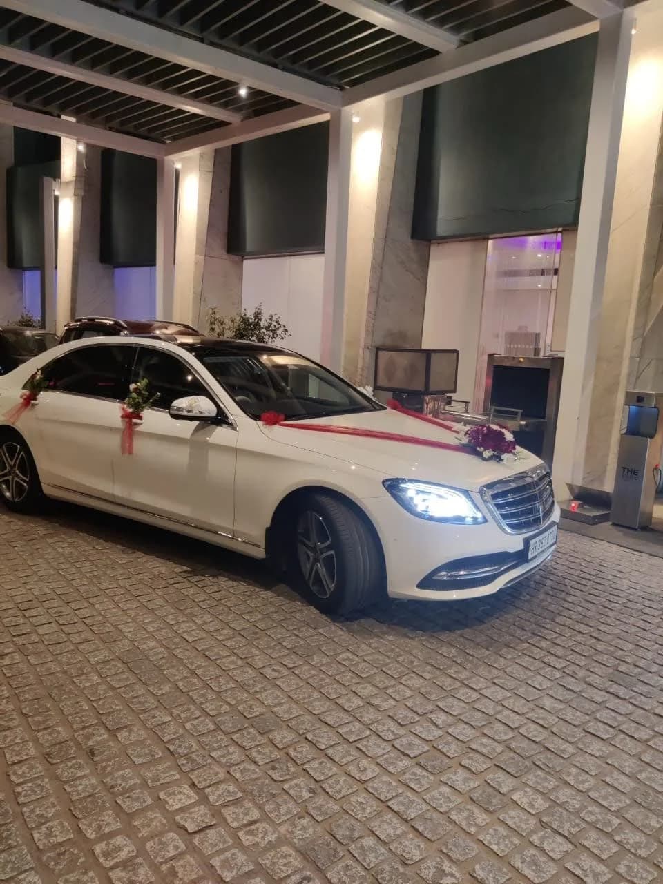 White Mercedes-Benz wedding sedan with red ribbons outside a venue at night