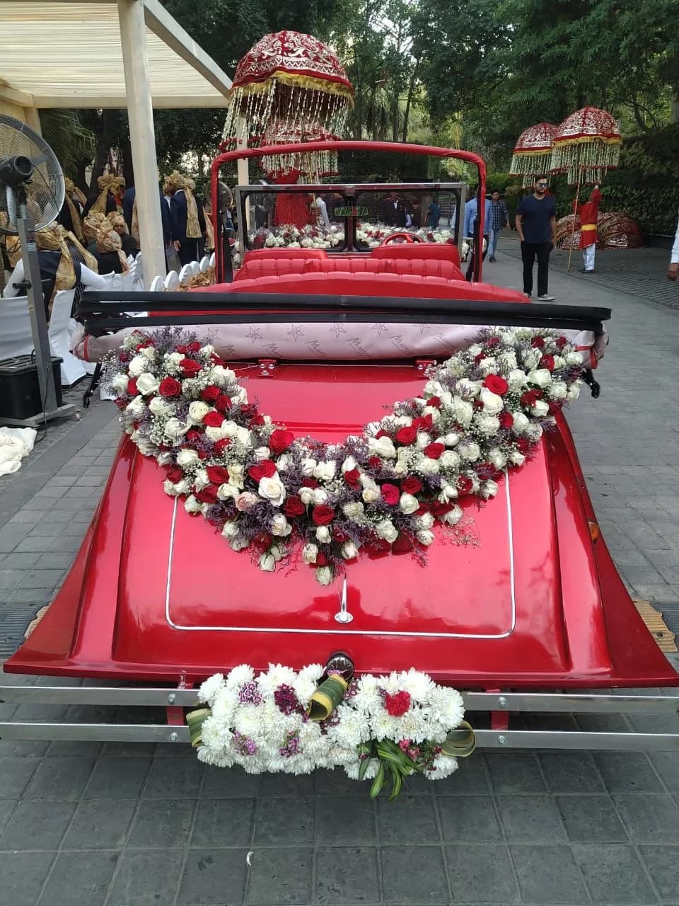 Red vintage wedding car with a red and white floral garland at the rear