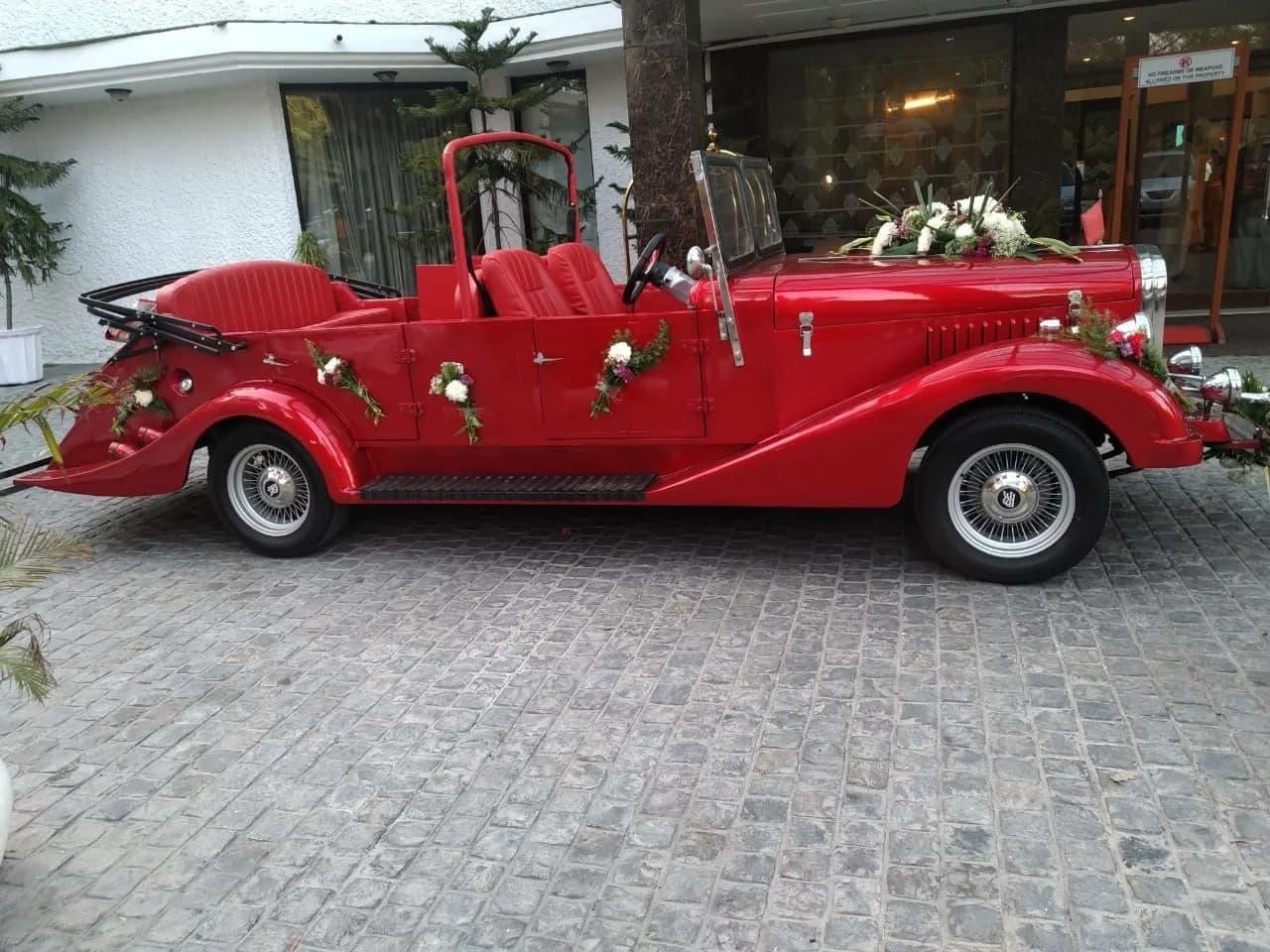 Red open-top vintage wedding car decorated with flowers outside a venue