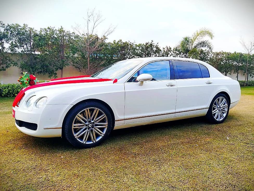 White Bentley wedding sedan with red bonnet ribbons on a lawn