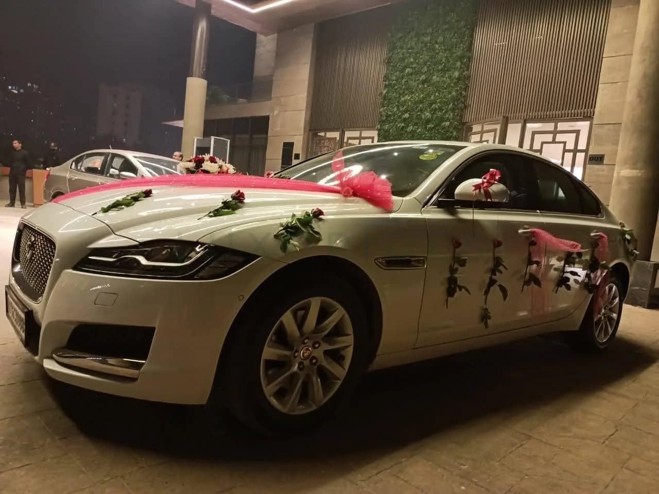 White Jaguar XF decorated with pink fabric and red roses at night